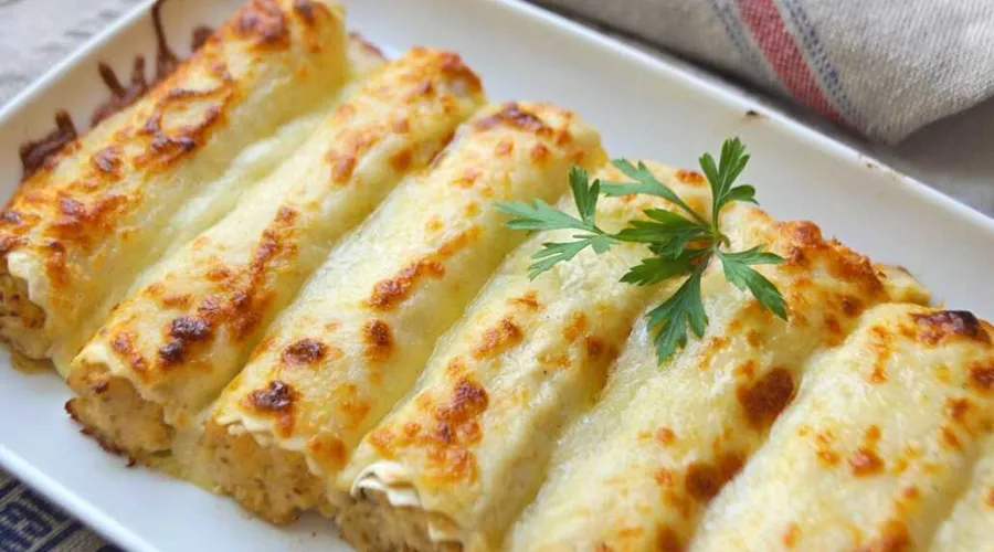 Overhead shot of a baking dish of Spanish canelones — pasta tubes bound in a golden-browned béchamel and parmesan crust, fresh from the oven.