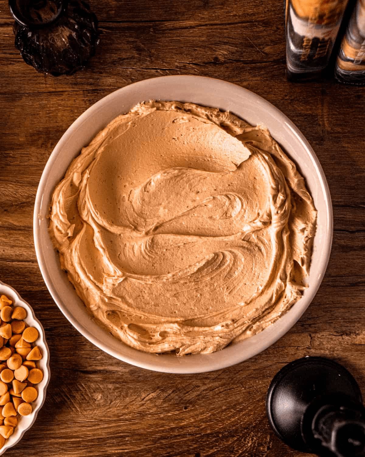 A ceramic bowl of butterscotch buttercream — pale caramel-colored, whipped to smooth glossy peaks.