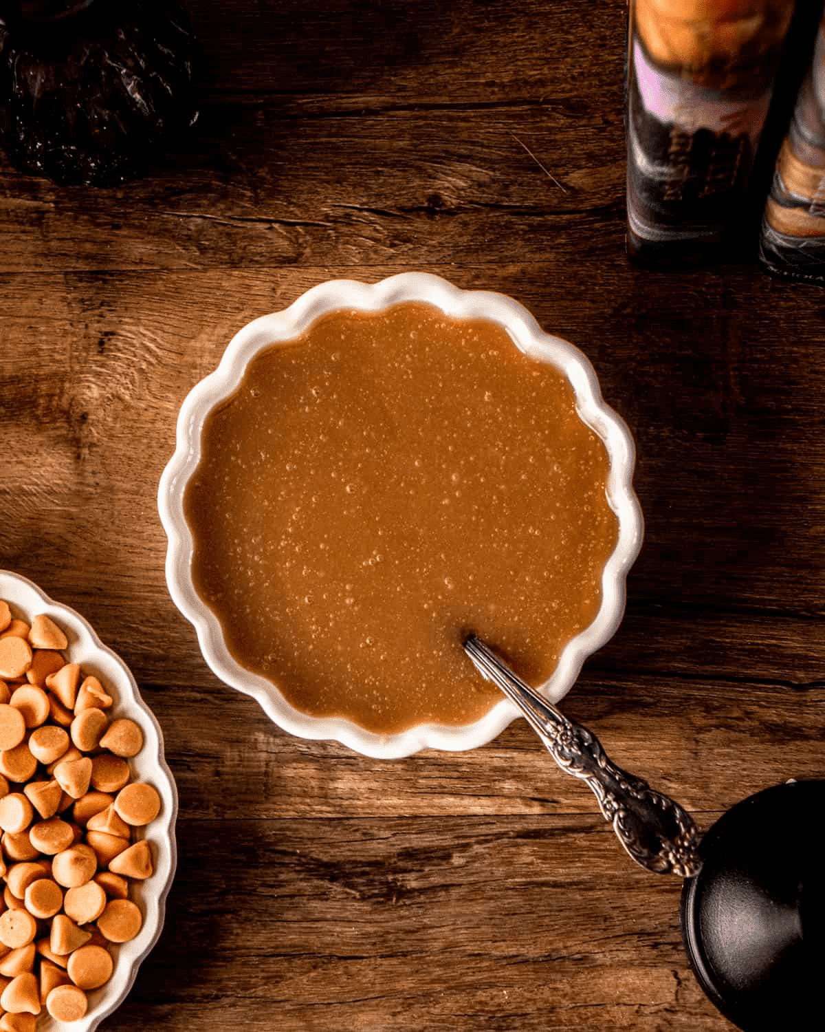 A small fluted dish of butterbeer caramel — deep amber, glossy, with an ornate silver spoon resting in it.